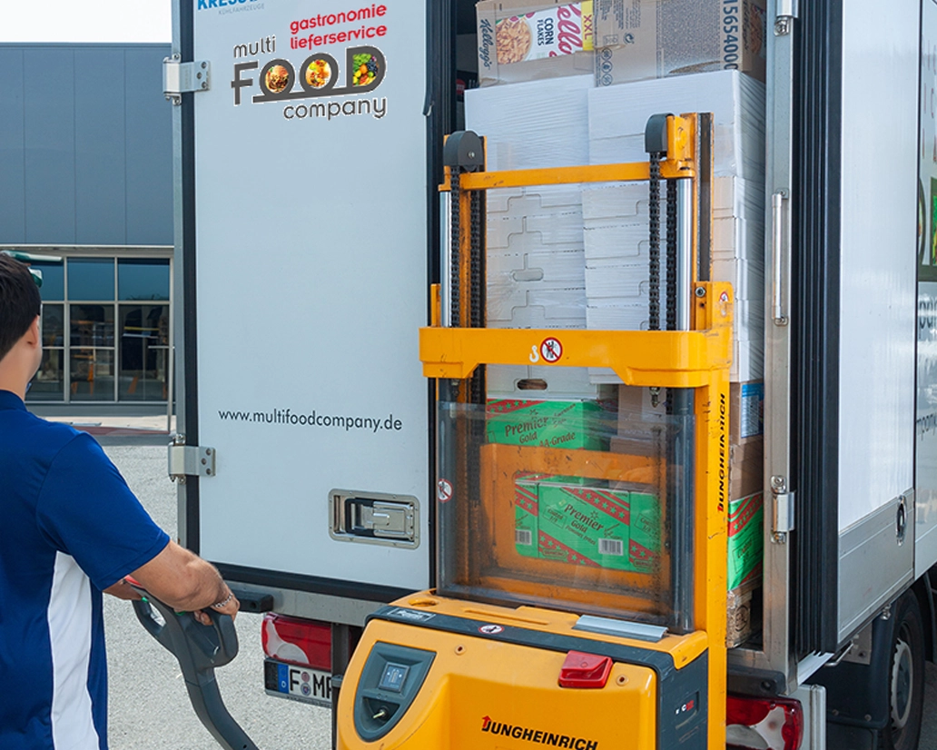 Ein Mitarbeiter belädt einen LKW der „Multi Food Company“ mit einem gelben Elektro-Gabelhubwagen – Prozess-Fotografie für Gastronomie-Logistik von FourMedia.