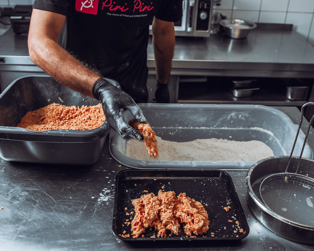 Ein Koch paniert frisches Hähnchenfleisch in der Küche von „Piri Piri“ in Frankfurt – authentische Prozessfotografie von FourMedia.